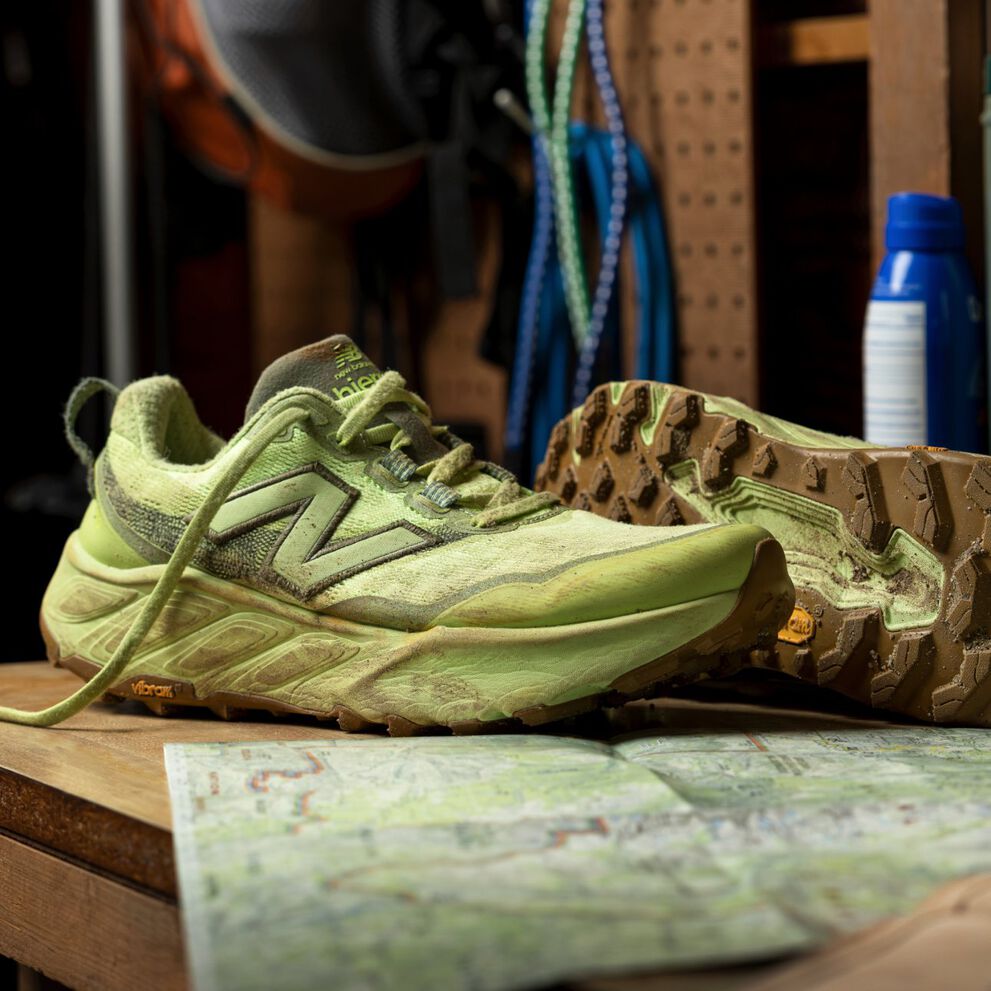 Pair of light green sneakers shown dusty and worn on a wooden workbench, with one shoe upright and the other flipped to display the sole, set beside a folded trail map. 